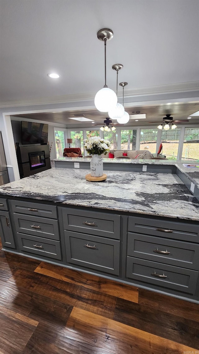 kitchen with light stone counters, gray cabinets, dark wood-style floors, decorative light fixtures, and crown molding