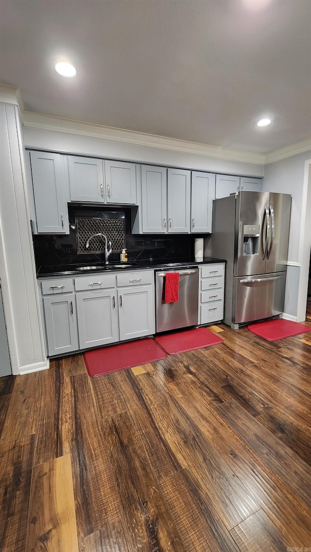 kitchen with a sink, appliances with stainless steel finishes, decorative backsplash, dark countertops, and dark wood finished floors