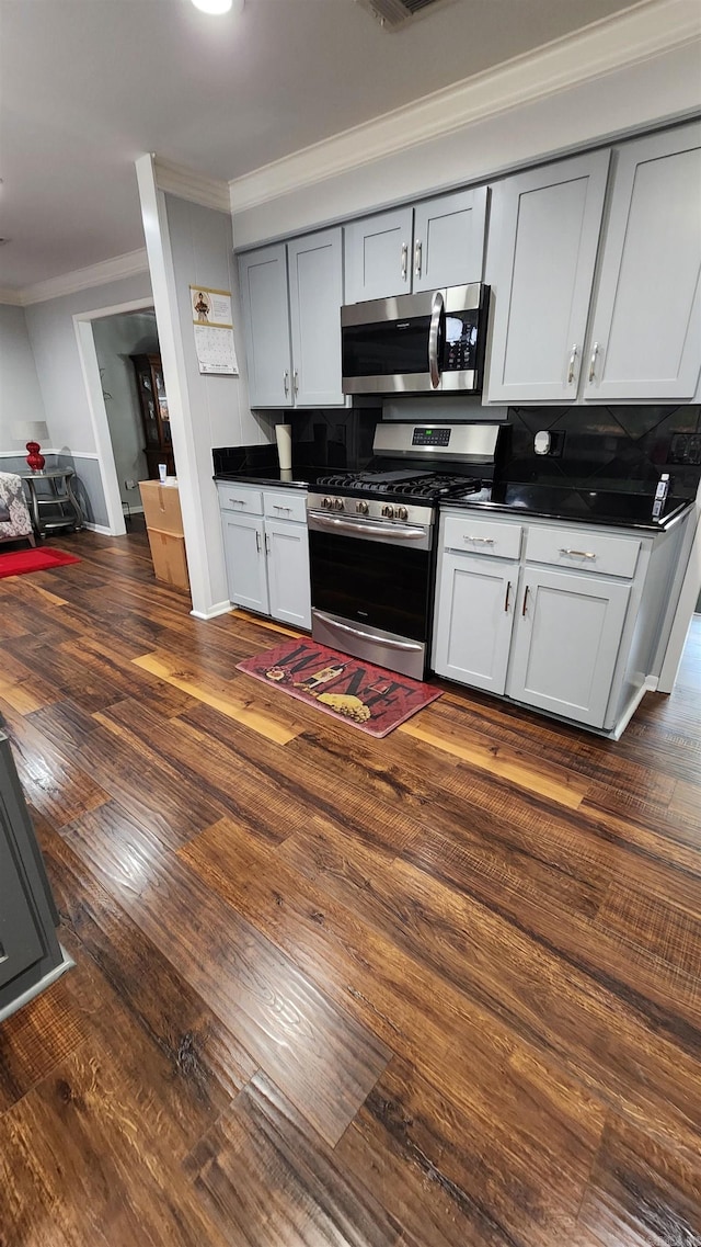 kitchen with ornamental molding, appliances with stainless steel finishes, dark wood-type flooring, and dark countertops