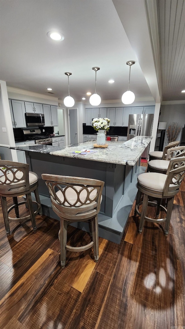 kitchen featuring a breakfast bar, dark wood-type flooring, light stone countertops, stainless steel appliances, and pendant lighting