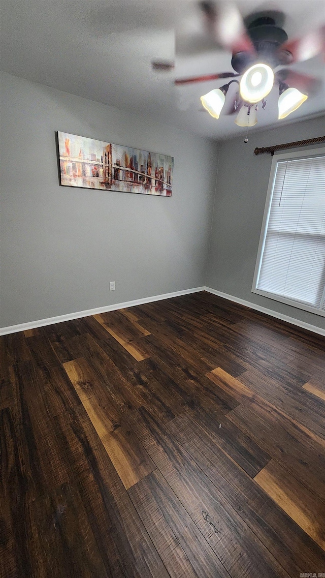 empty room featuring dark wood-type flooring, baseboards, and a ceiling fan