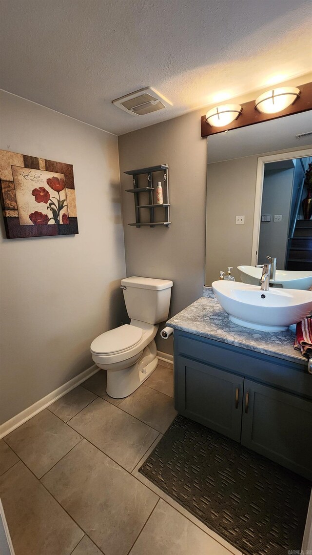 half bathroom with visible vents, toilet, a textured ceiling, vanity, and baseboards