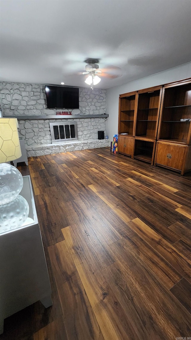 unfurnished living room featuring ceiling fan, a stone fireplace, and wood-type flooring