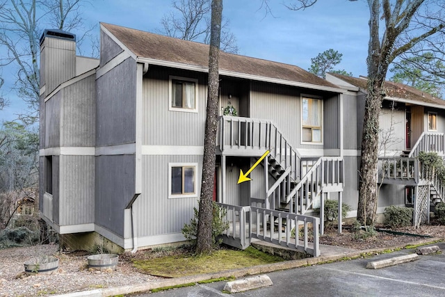 view of front of house featuring stairs, uncovered parking, a chimney, and roof with shingles