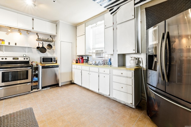 kitchen featuring white cabinetry, stainless steel appliances, light countertops, and ornamental molding