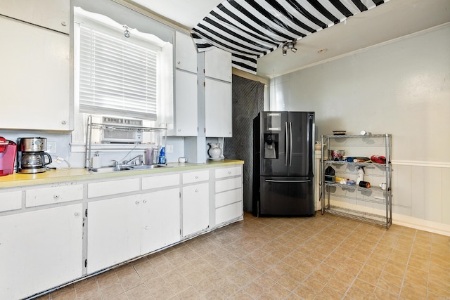 kitchen with a sink, refrigerator with ice dispenser, white cabinetry, light countertops, and wainscoting