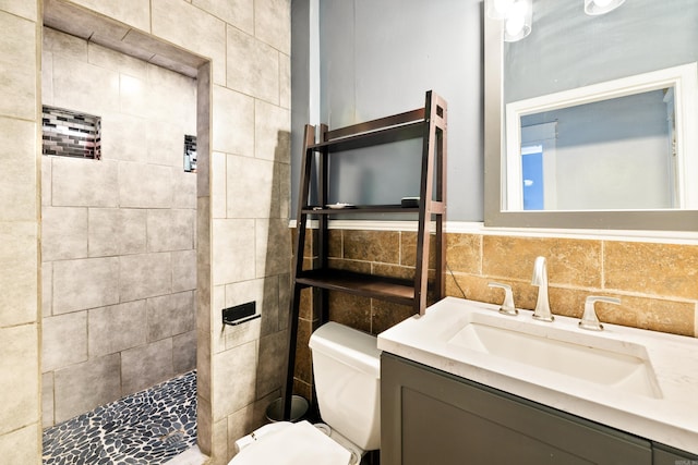 full bath with a tile shower, tile walls, toilet, and vanity