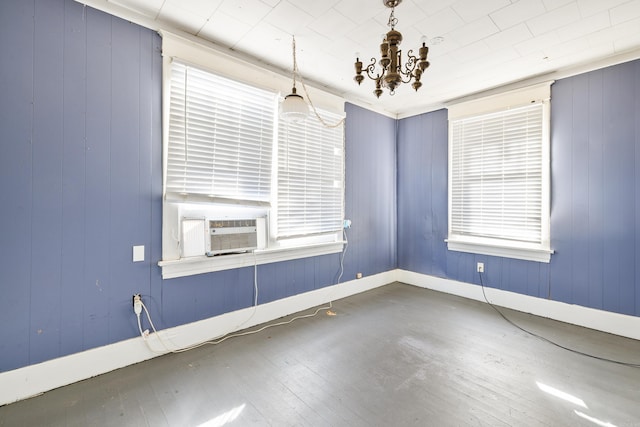 empty room featuring baseboards, wood finished floors, cooling unit, a chandelier, and a wealth of natural light