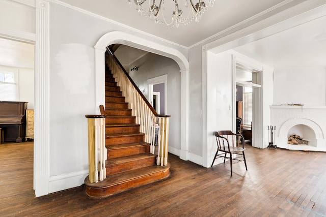 stairway with arched walkways, a notable chandelier, baseboards, ornamental molding, and hardwood / wood-style floors