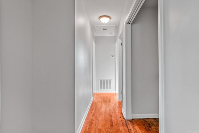 corridor with attic access, visible vents, light wood-style flooring, and baseboards