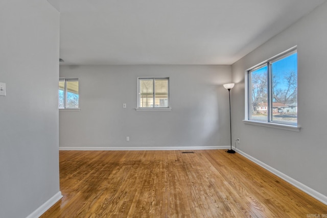 spare room with a wealth of natural light, visible vents, baseboards, and wood finished floors