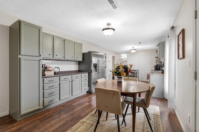 dining space with baseboards, visible vents, dark wood finished floors, and a textured ceiling