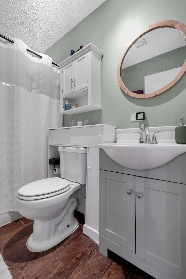 bathroom featuring a shower with shower curtain, toilet, a textured ceiling, vanity, and wood finished floors