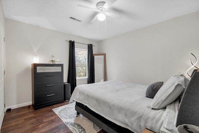 bedroom featuring baseboards, visible vents, dark wood finished floors, ceiling fan, and a textured ceiling