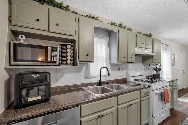 kitchen featuring stainless steel appliances, dark countertops, a sink, and under cabinet range hood