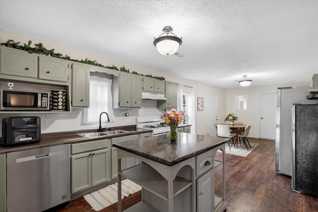 kitchen featuring appliances with stainless steel finishes, dark countertops, a sink, and under cabinet range hood