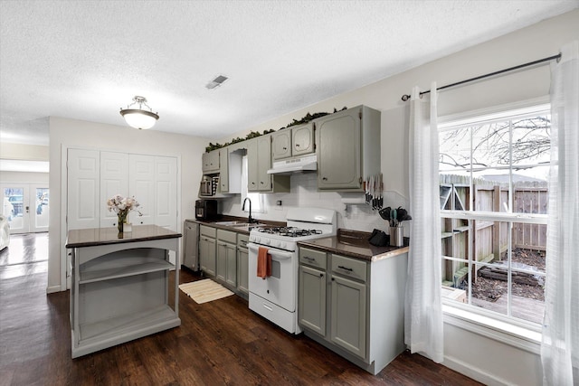 kitchen with dark countertops, under cabinet range hood, white gas range, and gray cabinetry