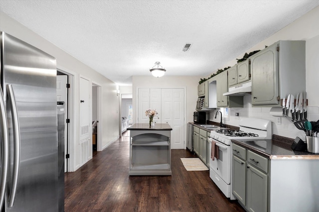 kitchen featuring white gas stove, dark countertops, a sink, stainless steel fridge, and under cabinet range hood