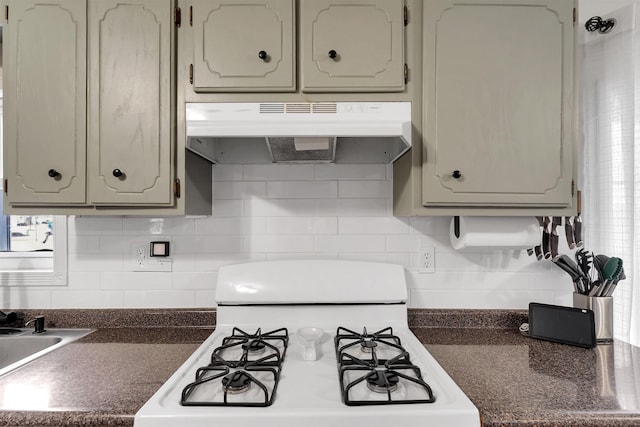 kitchen with dark countertops, white gas range oven, backsplash, and under cabinet range hood