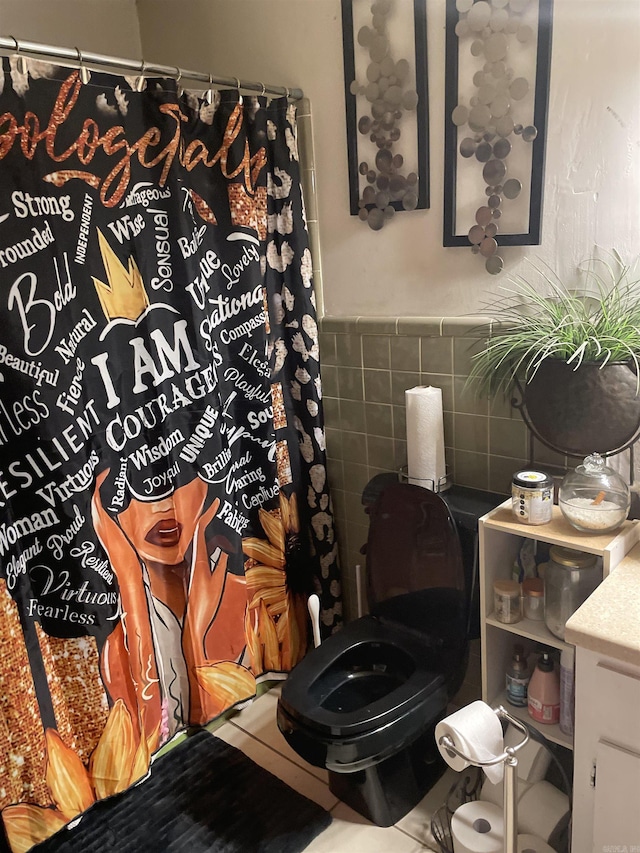 bathroom with a shower with shower curtain, wainscoting, toilet, vanity, and tile walls