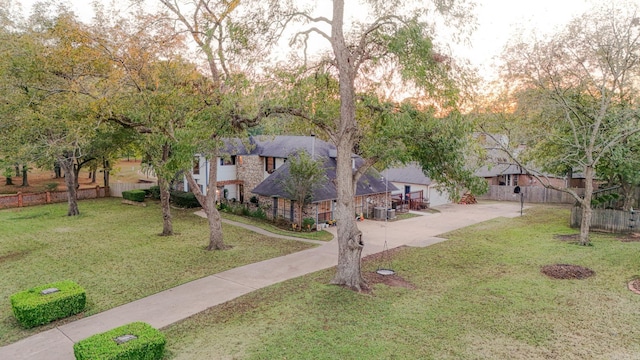 view of front facade featuring stone siding, fence, a front lawn, and concrete driveway