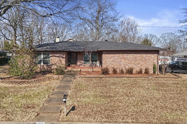 ranch-style house with a shingled roof, brick siding, a chimney, and a front lawn