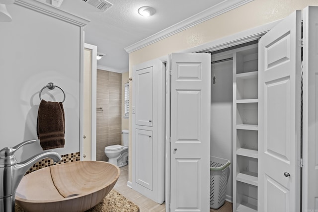 full bath with crown molding, tile walls, visible vents, toilet, and a textured ceiling