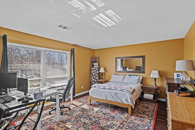 bedroom with visible vents, a textured ceiling, baseboards, and wood finished floors