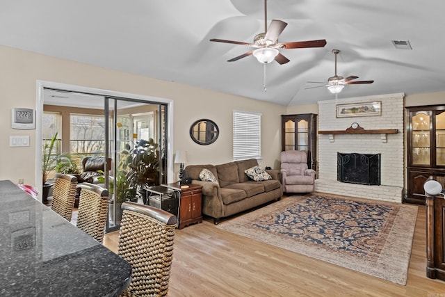 living area with light wood finished floors, lofted ceiling, visible vents, a brick fireplace, and ceiling fan