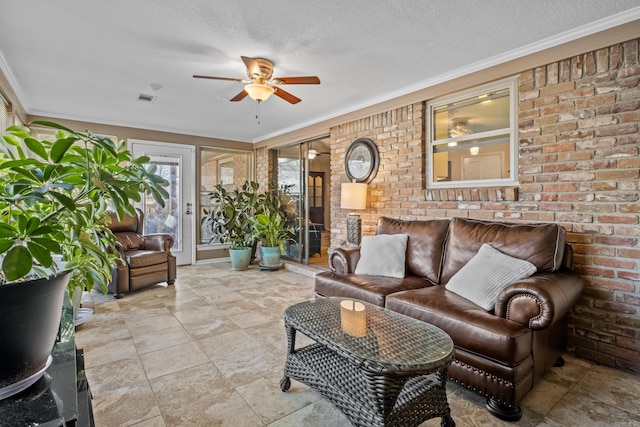 living area featuring a textured ceiling, ceiling fan, brick wall, visible vents, and ornamental molding