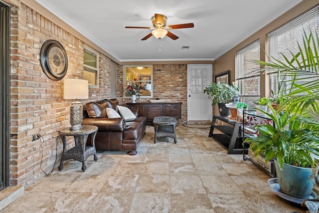 living area featuring brick wall, visible vents, ornamental molding, and a ceiling fan