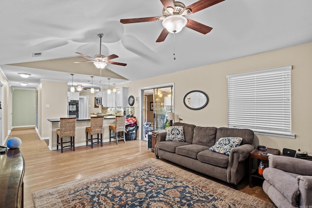 living room featuring lofted ceiling, visible vents, light wood-style floors, a ceiling fan, and baseboards