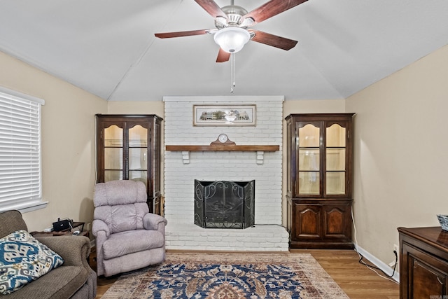 living area with baseboards, ceiling fan, wood finished floors, vaulted ceiling, and a brick fireplace