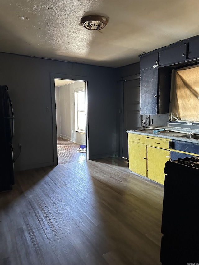 kitchen with light countertops, freestanding refrigerator, a textured ceiling, wood finished floors, and baseboards