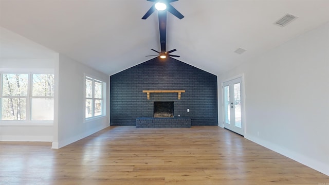 unfurnished living room with lofted ceiling with beams, a brick fireplace, a healthy amount of sunlight, and light wood finished floors