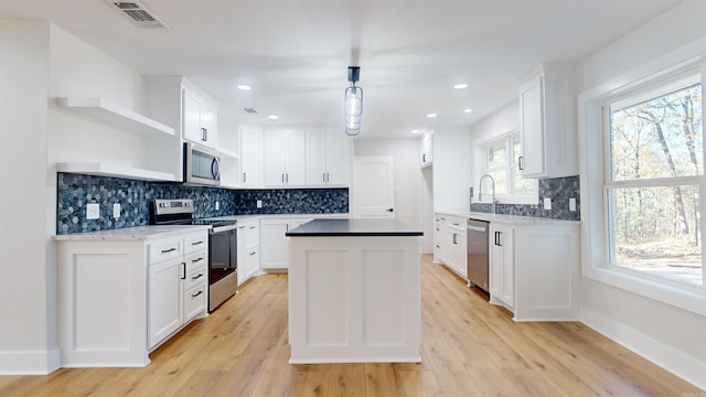 kitchen with a center island, open shelves, stainless steel appliances, visible vents, and light wood-type flooring