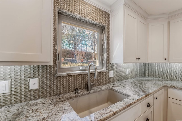 kitchen with tasteful backsplash, white cabinetry, a sink, and light stone countertops