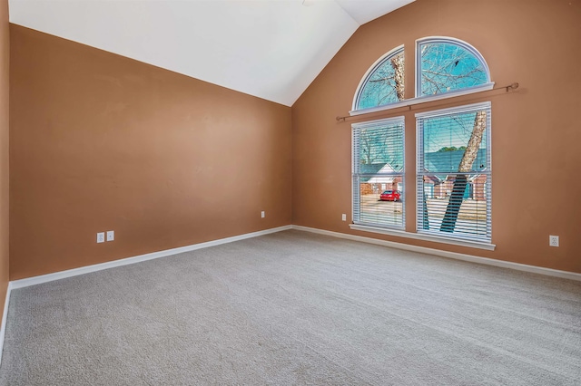 carpeted spare room featuring high vaulted ceiling and baseboards