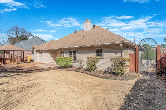 back of property with roof with shingles, a chimney, a gazebo, a gate, and fence