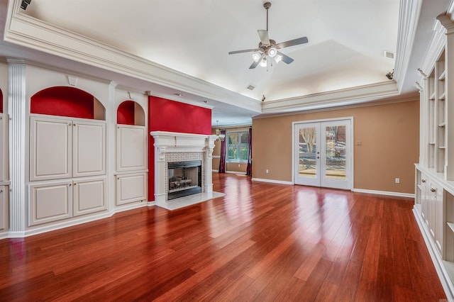 unfurnished living room featuring a tray ceiling, french doors, a fireplace, wood-type flooring, and ornamental molding