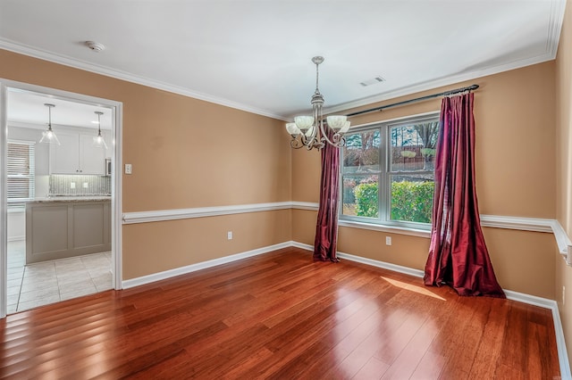 spare room featuring visible vents, ornamental molding, a chandelier, light wood-type flooring, and baseboards