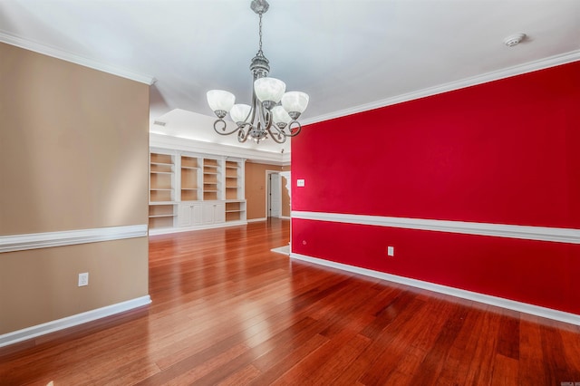 unfurnished dining area featuring a notable chandelier, an accent wall, wood finished floors, baseboards, and crown molding