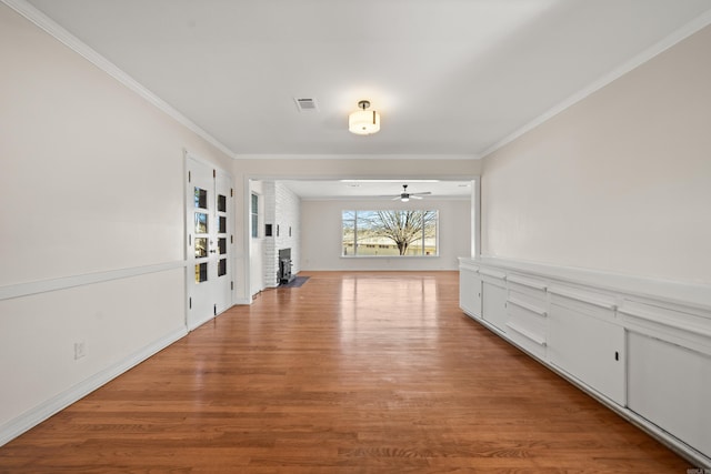 unfurnished room featuring ceiling fan, a fireplace, wood finished floors, visible vents, and ornamental molding