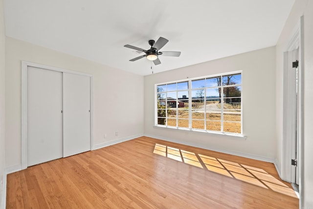 unfurnished bedroom with ceiling fan, a closet, light wood-style flooring, and baseboards