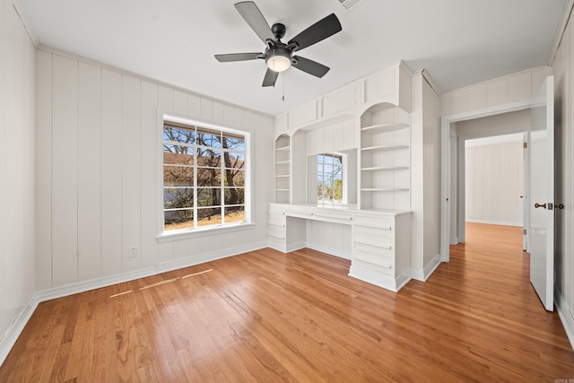 spare room with built in features, baseboards, a ceiling fan, light wood-style floors, and built in desk