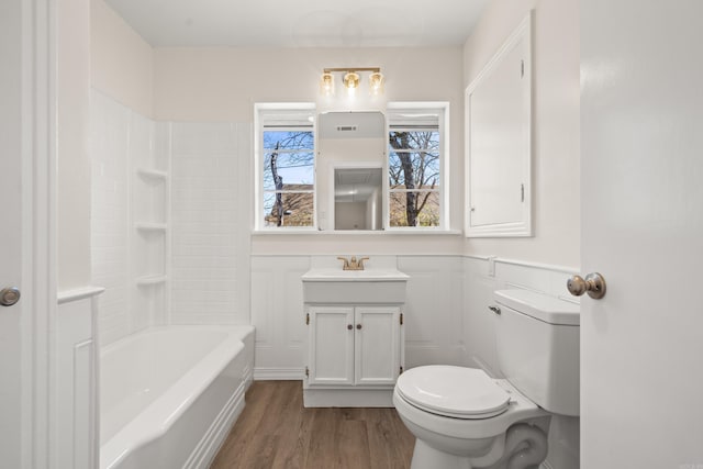 bathroom featuring toilet, a decorative wall, a wainscoted wall, wood finished floors, and vanity