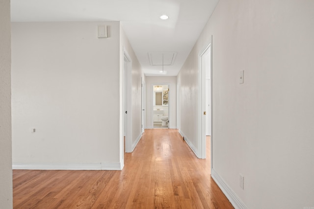 hallway featuring baseboards, attic access, and light wood-style floors