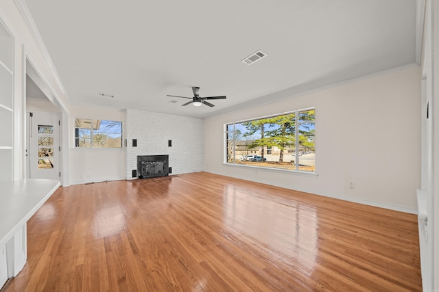 unfurnished living room with a ceiling fan, a brick fireplace, visible vents, and light wood-style floors