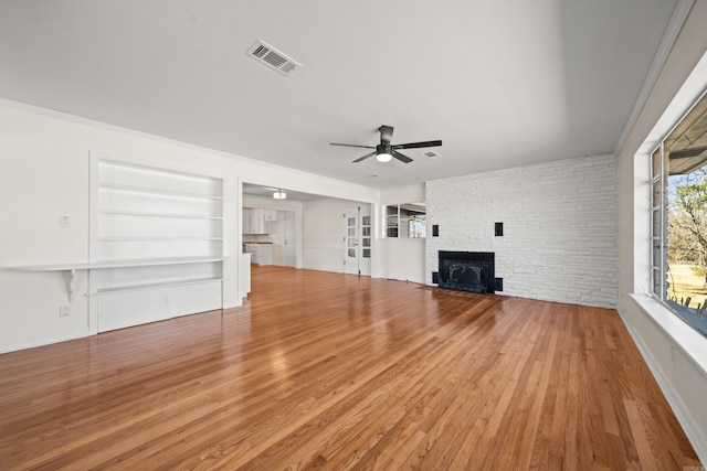 unfurnished living room featuring built in features, visible vents, ceiling fan, a stone fireplace, and wood finished floors