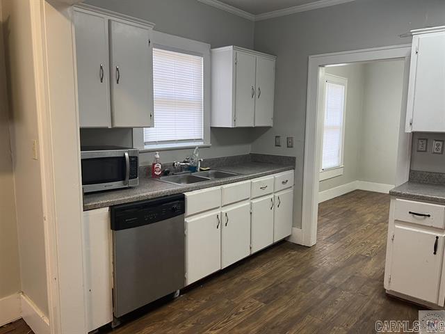 kitchen featuring white cabinets, dark wood-style floors, stainless steel appliances, crown molding, and a sink